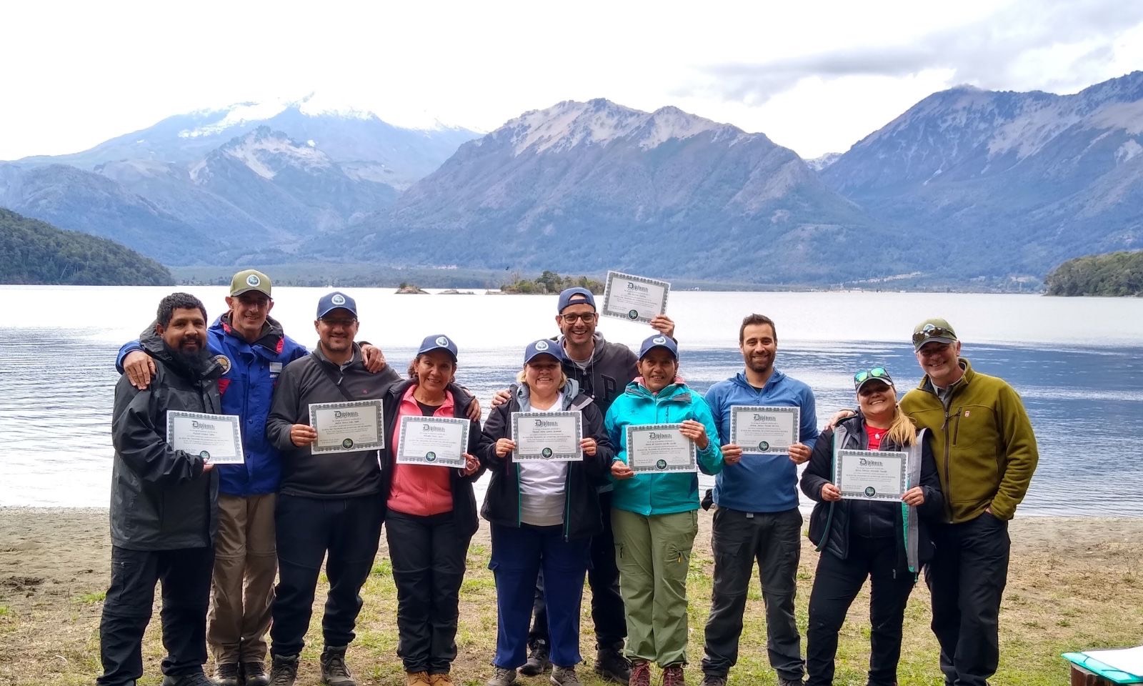 Grupo celebrando con diplomas frente a un lago y montañas en la Patagonia